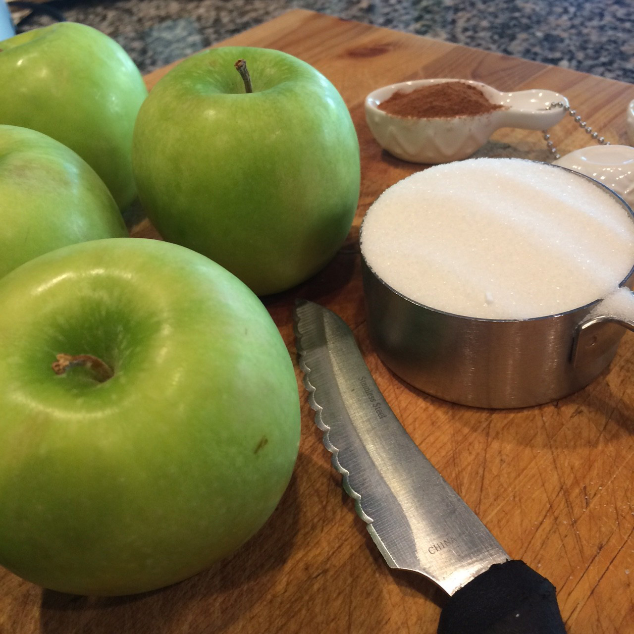 Green apples, sugar, cinammon on a cutting board
